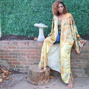 A woman models a flowing golden yellow Japanese kimono robe adorned with subtle olive branches, creating an elegant and nature-inspired design.