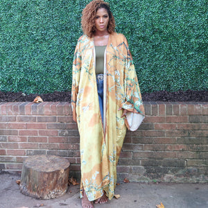 A woman models a flowing golden yellow Japanese kimono robe adorned with subtle olive branches, creating an elegant and nature-inspired design.