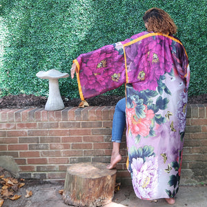 A woman models a flowing purple Japanese kimono robe adorned with flowers and golden yellow trim, fully lined for a luxurious and elegant design.