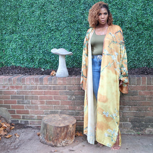 A woman models a flowing golden yellow Japanese kimono robe adorned with subtle olive branches, creating an elegant and nature-inspired design.