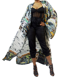 A woman models a luxury Japanese kimono robe in white with black trim, featuring subtle yellow and green tones with an abstract urban skyline design.