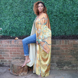 A woman models a flowing golden yellow Japanese kimono robe adorned with subtle olive branches, creating an elegant and nature-inspired design.