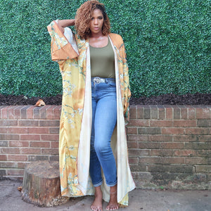 A woman models a flowing golden yellow Japanese kimono robe adorned with subtle olive branches, creating an elegant and nature-inspired design.