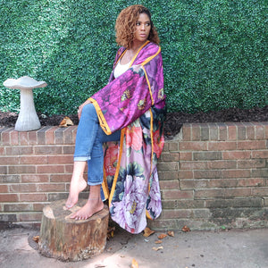 A woman models a flowing purple Japanese kimono robe adorned with flowers and golden yellow trim, fully lined for a luxurious and elegant design.