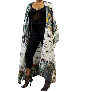 A woman models a luxury Japanese kimono robe in white with black trim, featuring subtle yellow and green tones with an abstract urban skyline design.