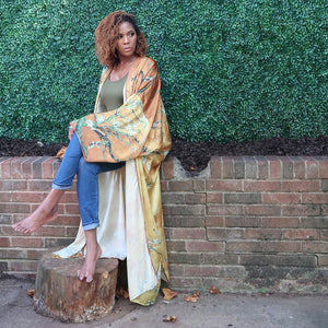 A woman models a flowing golden yellow Japanese kimono robe adorned with subtle olive branches, creating an elegant and nature-inspired design.