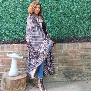 A woman models a flowing kimono jacket in black, grey, and white with a hood and a trim adorned with a horse and carriage motif, blending chic design with grace.